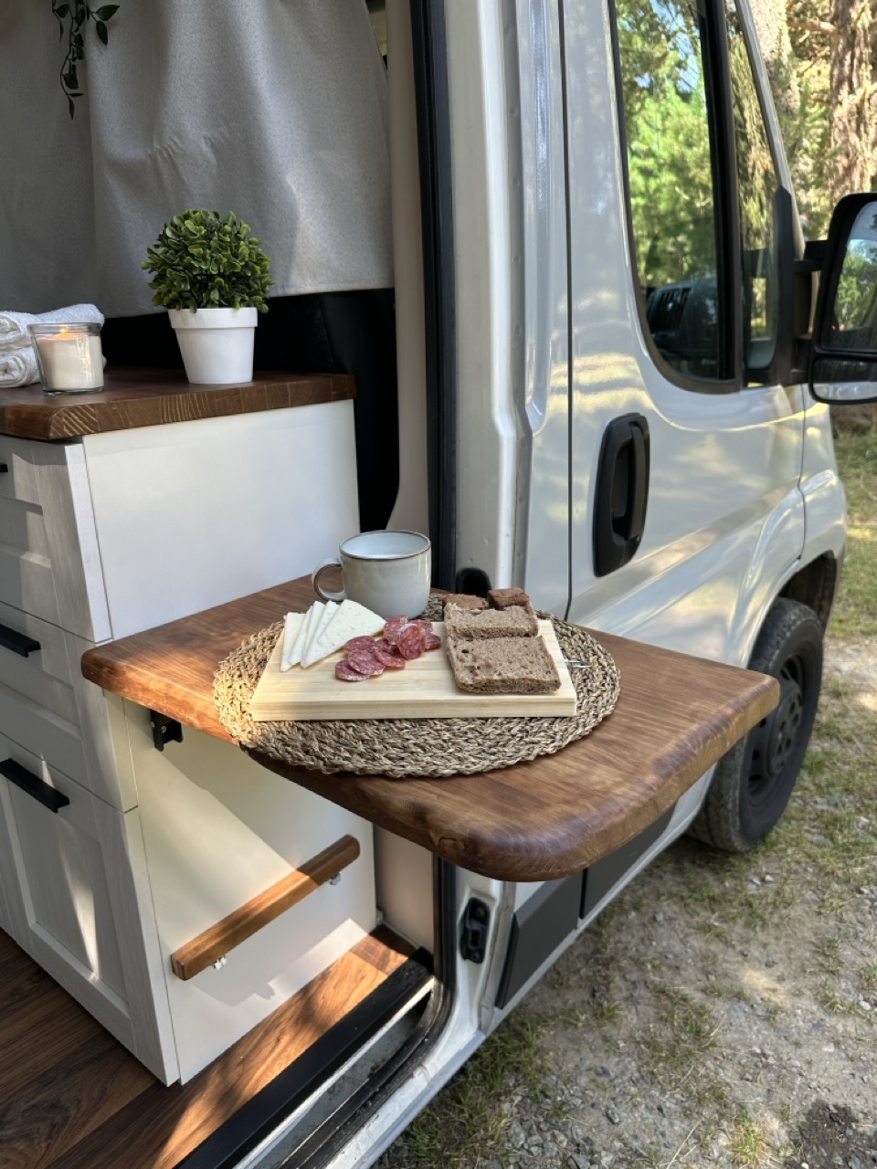 Mesa plegable de la camper con una tabla de quesos y embutidos, en el bosque